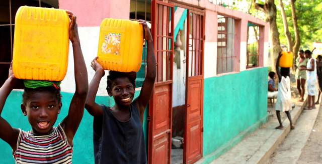 Children in Haiti are Carrying Yellow Water Jugs and Smiling at Camera
